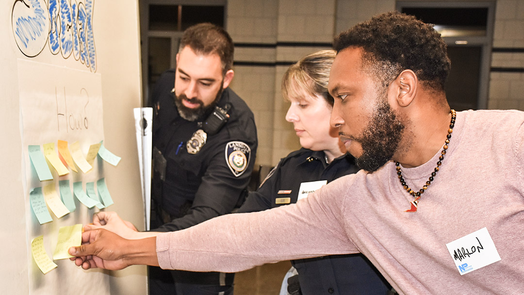 A man and two police officers stand around a board on post-it notes